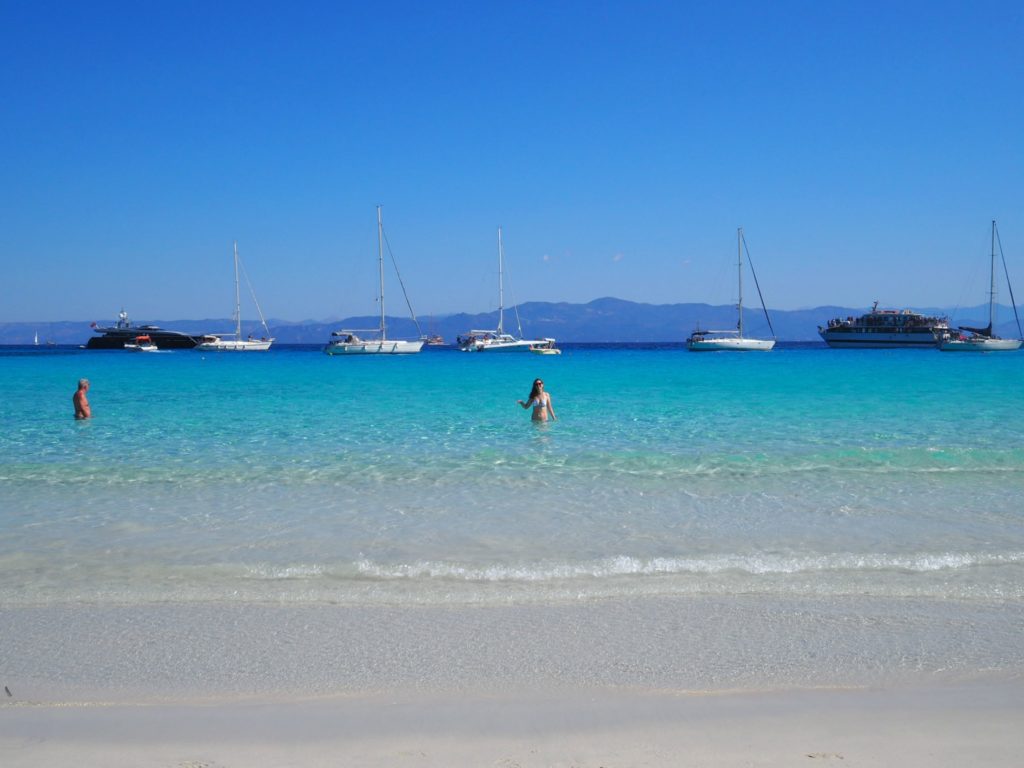 Turquoise blue sea with two people standing waist deep in water at Voutoumi beach. Copyright©2018 mapandfamily.com 