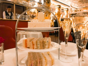 Glasses of champagne and a stand of cakes in a glittering room at the Cafe Royal.Copyright ©2019 mapandfamily.com