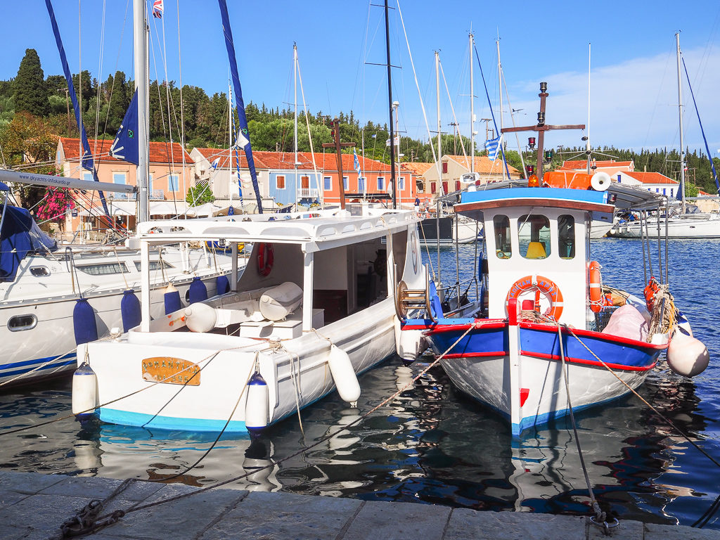 Fiscardo village. View of brightly coloured fishing boat and modern cruisers in harbour. Copyright ©2020 mapandfamily.com