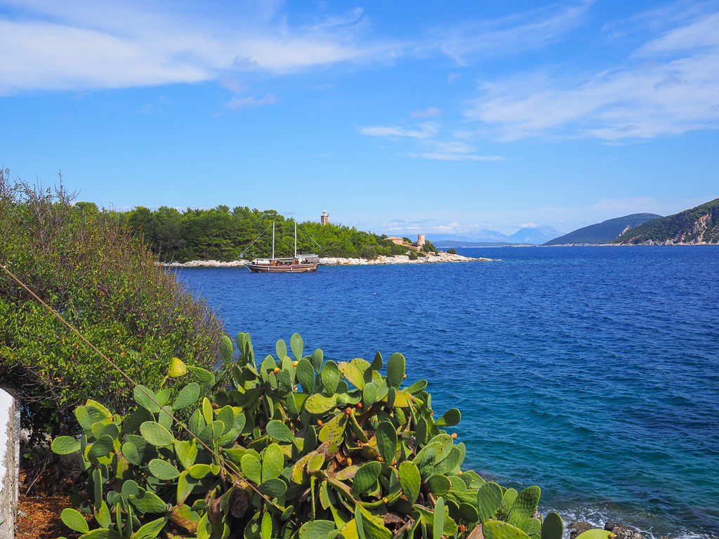 Fiskardo Kefalonia. View of peninsula with two lighthouses and traditional ship passing by. Copyright ©2020 mapandfamily.com