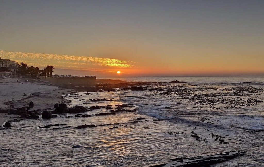 Cape Town sunset: pale apricot sunset over the sea  and reflected in water, viewed from Sea Point beach. Copyright@2024 reserved to photographer via mapandfamily.com 