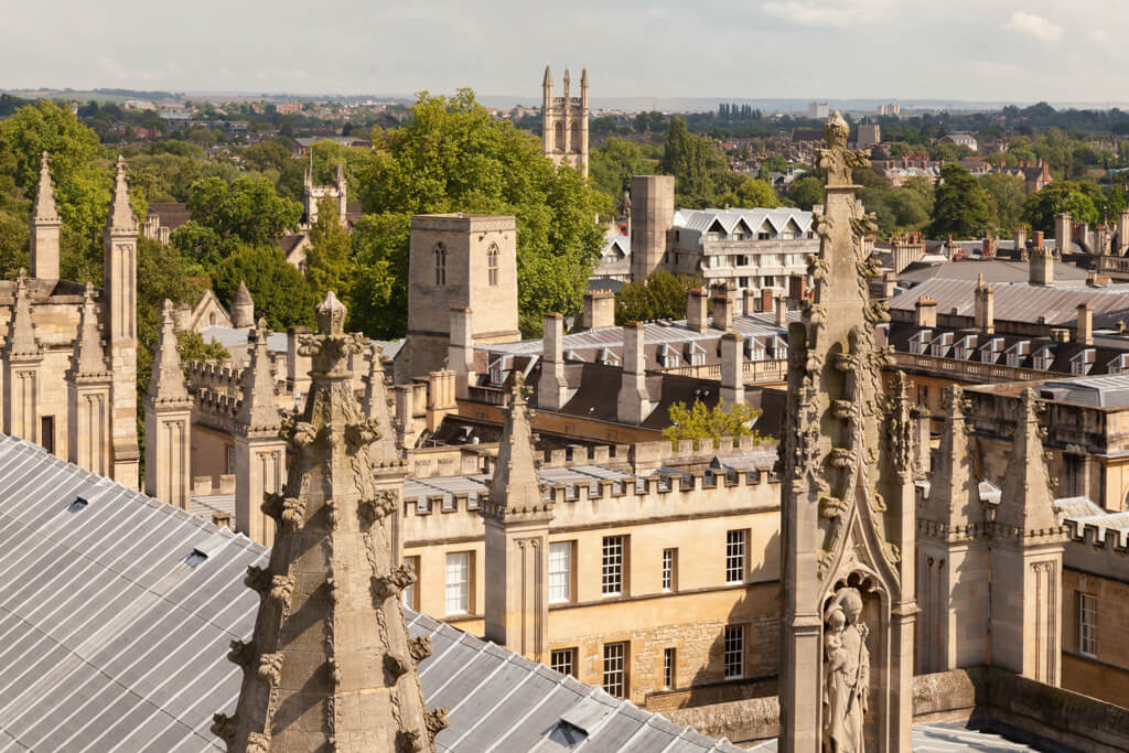 The skyline of Oxford with many spires and turrets along with mature green trees.
