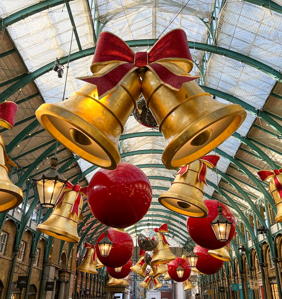 Covent Garden Christmas decorations: gigantic bells and giant baubles hanging from roof of Market building. Copyright@2024 mapandfamily.com