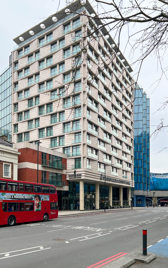 Modern hotel block with red London bus approaching on road outside. Copyright@2025NancyRoberts