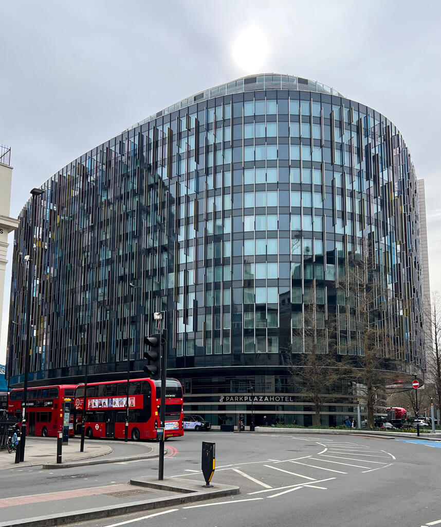 Large modern hotel overlooking road with red London bus passing by. Copyright@2025NancyRoberts