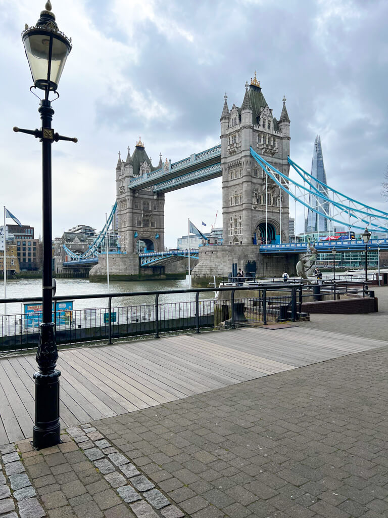 A view of Tower Bridge with blue painted detailing, the Shard tower in background and a traditional streetlamp in foreground. Copyright@2025NancyRoberts