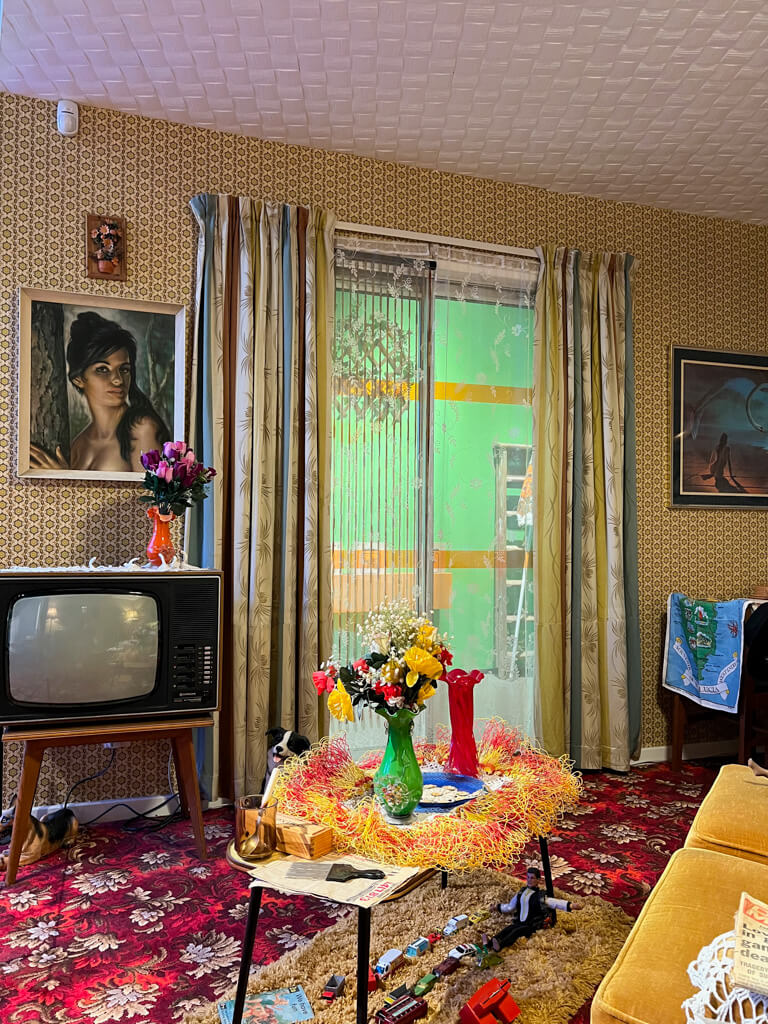 A brightly decorated front room with a boxy TV and flowery carpet. Copyright@2025 NancyRoberts