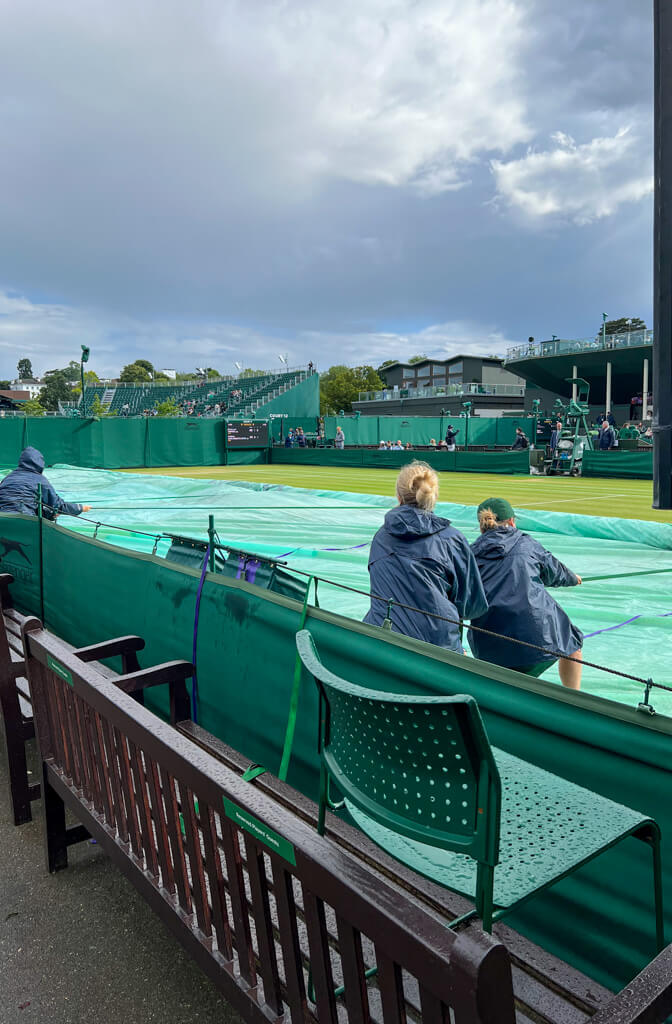 Pulling the green waterproof covers off an outside grass court to enable play after rain. Copyright@2025 NancyRoberts