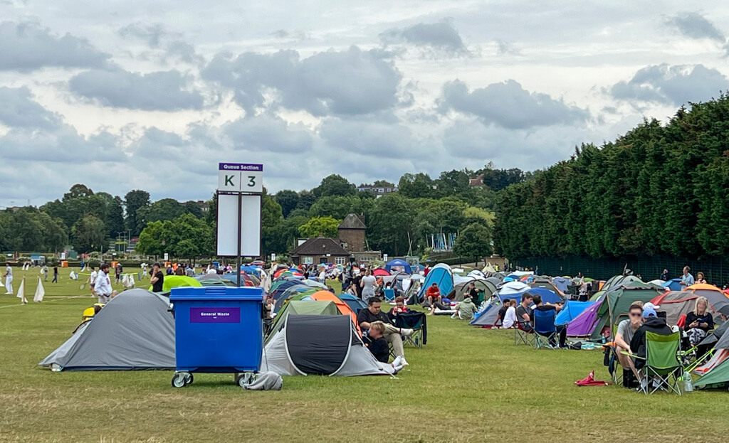 The Wimbledon Queue: lines of small coloured tents and people sitting on camping stools in parkland. Copyright@2025NancyRoberts